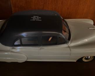 Promotional Gray Car Bank — Stamped-metal wind-up toy car with cream body and black roof; key-wind mechanism and metal base plate are visible. The piece shows age-appropriate wear including paint loss at bumpers and light surface scratches on the underside near the axle mounts. Solid collectible for display or repair — measures like a mid-20th-century pressed tin toy with simple rubber tires and working wind-up slot. No maker name legible from photos.