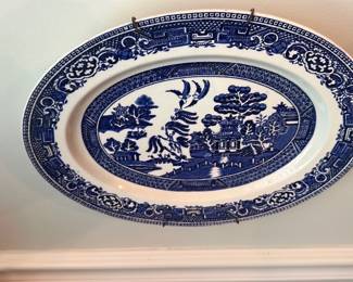 Blue Willow Oval Serving Platter — Classic Blue Willow transferware oval serving platter featuring the traditional chinoiserie landscape pattern in blue on white. Made of ceramic/porcelain with a wide decorative border and central scene, it's suitable as a serving piece or wall display in the living room. Measures approximately 14.5 inches long and 10.5 inches wide, a practical size for serving or decorative use. In good condition with no visible chips or cracks from images; shows light surface wear consistent with use.