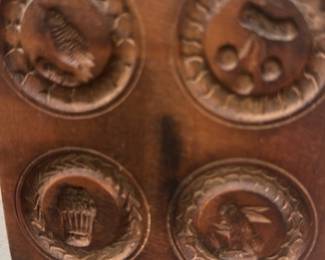 Butter press — Small carved wood wall plaque featuring four circular medallions with relief motifs (bird, fruit/berries, basket, and seated figure). The warm brown finish shows light surface wear and a dark vertical mark down the center consistent with age and hanging; overall solid and decorative for a sun room or small gallery wall. Hand-carved look suggests folk or decorative craft work rather than a stamped mass-produced piece. Measures small and lightweight, suitable as an accent or paired with similar plaques.