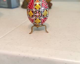 Handpainted Decorative Egg — Small handpainted decorative egg with geometric folk-style motif in red, yellow and black on a white ground, mounted on a small three-leg brass-tone stand. Eye-catching tabletop accent for a curio shelf or dresser; the paintwork appears hand-applied with fine line detail. No maker's marks visible in photos; shows light surface wear consistent with age but no obvious chips or cracks. Compact and display-ready as shown.