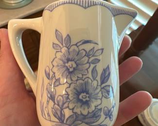 Mayer China Co. Blue Floral Pitcher — Small ceramic pitcher by Mayer China Co., marked "Mayer China Co. Beaver Falls PA U.S.A. 482" on the base. Cream background with hand-painted or transfer blue floral decoration and scalloped rim detail; comfortable handle and pour spout make it useful as a creamer or small pitcher. Mayer China produced utilitarian dinnerware mid-20th century and pieces like this are modestly collectible; this example shows light surface wear and glaze crazing consistent with age but no visible chips or cracks. Measures small enough for tabletop use or display with other transferware.
