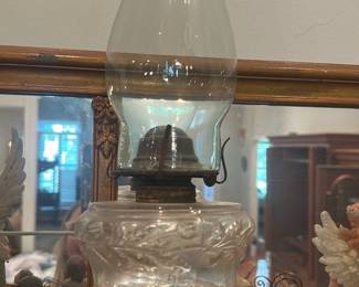 Glass Oil Lamp with Chimney — Clear pressed-glass oil lamp with a tall glass chimney and decorative molded font. The lamp has a metal burner assembly and a patterned glass reservoir with a clear stem; photos show light surface wear and patina on the metal burner but no obvious cracks in the glass. A classic functional decorative lamp suitable for mantel or sun room display; measures compactly and appears complete except fuel and wick are not included.