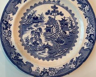 Blue Willow Transferware Plate — Classic blue willow transferware charger/plate featuring the traditional chinoiserie landscape with pagodas, bridge and willow tree. Decorated in deep blue on white ceramic with detailed border and scalloped rim, suitable as wall decor in the living room. Approximate overall diameter and practical display size provided below; lightweight enough to hang but sturdy ceramic construction. Plate shows crazing consistent with age and use but no visible large chips or cracks from the photo; sold as decorative vintage-style dinnerware.