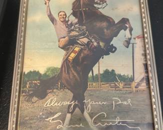 Signed Photo-Look Print 'Always yours Pa — Framed color photograph print showing a smiling rider on a rearing horse with a white handwritten-style inscription across the lower image reading "Always yours Pal" and a signature that appears as "L.... C..." (signature partly legible in photo). The piece is in a simple silver-tone metal frame with decorative inner border; glazing intact but image shows light age toning and minor surface spots. Good decorative condition for display; frame has light wear consistent with age.