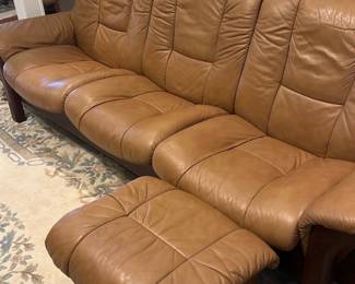 Stressless Tan reclining Leather Sofa — This Stressless tan leather three-seat sofa with matching ottoman offers Scandinavian comfort and quality craftsmanship. Upholstered in warm tan leather with tufted seat and back cushions, it sits on dark wood frame and legs with Stressless maker badge. Comfortable for living room use; overall dimensions estimated to fit a standard three-seat sofa and ottoman. Shows gentle wear to leather consistent with normal use but no major tears or stains visible.