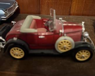 Diecast Model A Car — Small diecast classic roadster model in red with cream interior and yellow wire-style wheels. Metal body with plastic trim and chrome-plated bumpers; underside shows molded suspension detail and factory markings. Good overall condition with minor surface wear consistent with display; no broken parts visible in photos. Approximately pocket-size collectible suitable for display on a shelf or in a curio cabinet.