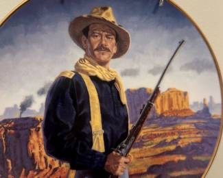 Western Soldier Decorative Plate — Decorative round collector plate depicting a rifle-bearing western soldier in uniform against a canyon landscape. Plate has a gilt rim and is wall-mounted on small metal hangers; artist signature visible at lower edge but not fully legible in photos. Good overall condition with minor surface glare visible in photos; no obvious chips or cracks. Ideal for Western-themed decor or plate collectors who appreciate pictorial landscape plates.