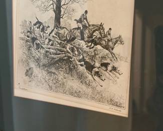 Framed Fox Hunt Engraving — Classic black-and-white fox hunt engraving matted and framed with gold wood frame and dark green mat. The print shows riders and hounds jumping a fence; signature appears lower right (hard to read in photos). Overall size suitable for hallway or living room display; frame shows light surface wear and mat has minor age toning. Glass is intact and piece is in good vintage condition with no visible tears to the print.