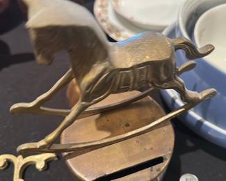 Brass Rocking Horse Figurine — Heavy brass rocking-horse figurine with stylized molded details and a slotted round base as shown. Solid brass construction gives it a warm patina and small surface age spots consistent with light wear; no obvious breaks or repairs visible in the photos. A decorative tabletop accent for a mantel, shelf, or nursery display; measures compactly and feels substantial in hand. Condition shows expected surface wear and patina but no structural damage.