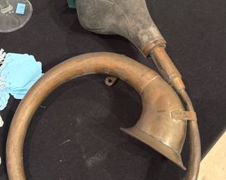 Brass Bugle Horn — Heavy brass bugle-style horn with a cloth or leather-covered rubber bulb for hand-squeeze signaling. The instrument is a circular coiled horn with patina and surface wear consistent with age and use; bulb shows discoloration and some surface grime. Functional as a decorative signal horn or prop; no visible maker's marks in photos. Measures approximately as shown below.