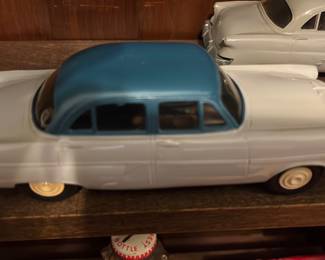Green Top Toy Car — Metal diecast classic four-door sedan model with a two-tone blue roof and light gray body. Stamped steel chassis shows surface rust consistent with age; wheels and axles are intact and the painted body has light wear but no major dents visible. Good display piece for collectors of mid-century car models or as a shelf accent; measures small and is easy to display. Condition shows expected play/use wear and oxidation on the underside.