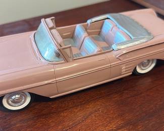 Pink Classic Convertible Toy Car — Vintage-style pink convertible toy car with silver trim and whitewall wheels; a decorative desk or shelf piece from the office room. The plastic/resin model features detailed interior seating for four, a wraparound windshield, molded hood ornament and textured front bumper. Approximately small collectible size suitable for display; shows surface scratches and light wear on painted areas and chrome trim consistent with age. Sold as a decorative model in fair condition with cosmetic wear but no major breaks visible.