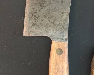Wood-Handled Cleaver Knife — Sturdy cleaver-style butcher knife with a wide carbon-steel blade and a three-rivet wood handle. Blade shows surface patina and light pitting consistent with age and use but appears solid and usable after sharpening and cleaning. Rounded hole near the spine for hanging; handle is intact with normal wear to finish. Good functional piece for butchery or as a rustic kitchen display.