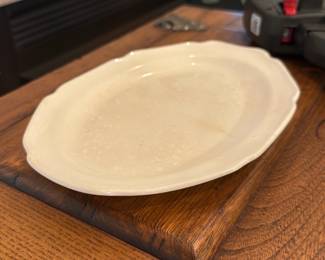 Cream Ceramic Serving Platter — Large cream-colored ceramic serving platter with a gently scalloped rim and raised concentric banding. The piece shows typical crazing/discoloration and a faint brownish stain on the underside rim visible in photos; otherwise no visible chips or cracks on rim edges. Useful as a serving platter or decorative centerpiece; sturdy, heavier ceramic construction with a glazed finish.