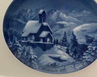 Christmas 1975 Collector Plate — This blue-and-white collector plate titled "Christmas 1975" depicts a snowy chapel scene with pine trees and figures in a serene winter landscape. The ceramic plate is decorative and likely intended for holiday display in the living room; the seller notes location as Living Room. Approximate diameter and weight are provided below; plate shows light surface wear consistent with display but no visible chips or cracks from the photo. A nice seasonal collectible for holiday decor or a themed plate collection.