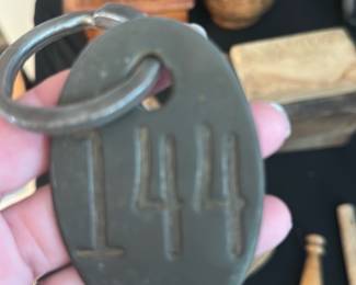 Oval Key Tag 144 — Solid oval brass key or locker tag stamped with raised numerals "144" and fitted with a thick iron split ring. The piece shows honest surface wear and patina consistent with age and handling but is structurally sound; no cracks or breaks visible. Good collectible or decorative piece for keys, industrial decor, or as a numbered lot marker. Measures small and lightweight — see dimensions below.