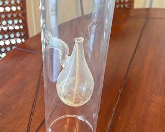 Tear Drop Lamp — Delicate handblown clear glass sculpture shaped like a raindrop with an attached curved spout, displayed inside a clear acrylic cylinder in the photos. The piece appears to be mouth-blown with tiny internal bubbles and light surface wear and spotting consistent with age or previous display. Lovely as a small tabletop accent or part of a glass collection; lightweight and fragile so handle with care. Condition: good overall with visible surface spotting and minor wear; no obvious large chips or cracks visible in the photos.
