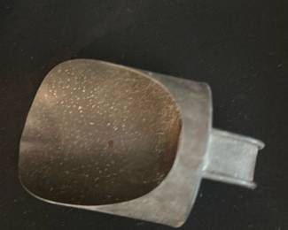 Metal Measuring Scoop — Heavy metal measuring scoop likely used for dry goods or small batching tasks. Solid stamped-metal construction with a short squared handle and signs of age/oxidation across the surface; finish shows surface pitting and patina but no visible cracks or breaks. Compact, utilitarian piece suitable for kitchen use, workshop measuring, or display with other vintage tools. Condition shows wear consistent with age and regular use.