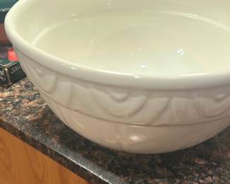 White Ceramic Mixing Bowl — Large white ceramic mixing bowl with an embossed swag and bead decorative border around the rim. Heavy, glazed earthenware construction shown in good used condition with light surface wear and no visible chips or cracks in photos. Useful for baking, serving, or as a display piece; pairs well with other colored nesting bowls visible in the images. Hand-wash recommended due to the glaze and thickness.