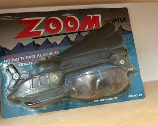 Zoom Copter Toy Helicopter — Zoom Copter toy helicopter in original blister card packaging; the card reads "ZOOM COPTER" and notes "NO BATTERIES REQUIRED" and "ZOOMS TO OVER 100 FEET." Plastic copter body marked "NAVY" with attached clear plastic dome and two large black rotor blades. Packaging shows shelf wear and some yellowing but item appears complete in package; unopened but age-related wear to card and plastic bubble.