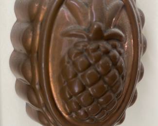 Copper Pineapple Jelly Mold — Decorative copper pineapple jelly or cake mold with embossed pineapple motif and hanging ring at top. Solid-appearing copper construction with scalloped outer edge and warm aged patina, suitable for wall display or kitchen decor. Measures approximately 8.5 inches tall by 6 inches wide and projects about 2 inches from the wall, a lightweight decorative piece. Good vintage condition with expected surface patina and minor surface wear consistent with age.