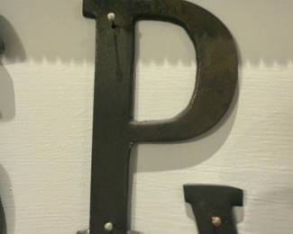 Metal Wall Letter P — Single freestanding metal wall letter 'P' with a dark painted finish and two small mounting nails visible on the face. The piece is a decorative signage letter suitable for wall mounting or craft projects; finish shows light surface wear and minor paint loss at edges consistent with age and use. Clean, simple serif form offers an industrial or farmhouse accent; sold as a single letter only. Measures approximately as shown below.