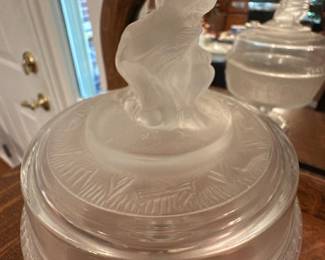 Frosted Glass Covered dish — Frosted glass covered urn or compote featuring a molded figural finial on the lid and an etched decorative band around the body. The piece appears pressed and frosted with clear and matte areas highlighting the relief pattern; photos show some light surface wear and typical handling marks but no obvious chips or cracks. Good decorative condition for display on a sideboard or in a curio; measures approximately as noted below.
