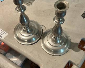 Pair Pewter Candlesticks — Pair of pewter-tone metal candlesticks with turned column design and round weighted bases. Each holds a standard taper candle; finish shows light surface wear and minor scuffs consistent with normal use but no visible dents. Solid-feeling decorative pieces that work well as dining or mantel accents and are easy to clean and display. Sold as the pair.