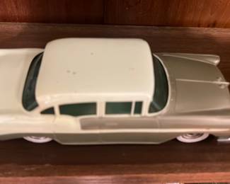 Green Cream Toy Car — Metal diecast model car in a two-tone pale green and cream finish with chrome-look trim and whitewall tires. The piece appears to be a decorative collectible or shelf model; underside shows simple stamped base and rolling wheels. Paint has small spots and light wear consistent with age and display; wheels roll but one rear wheel shows minor damage. Approximately 9 inches long and solid metal construction give it a substantial feel for display.