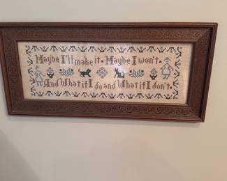 Framed Cross-Stitch Sampler — Framed cross-stitch sampler featuring a whimsical border and text reading "Maybe I'll make it. Maybe I won't. And what if I do and what if I don't" in muted blues and greens on a natural linen ground. The piece is mounted behind glass in a carved wooden frame with foliate tooling; stitching appears even and colors are intact. Ready-to-hang decorative needlework suitable for bedroom or hallway display with light surface wear to the frame consistent with gentle use.