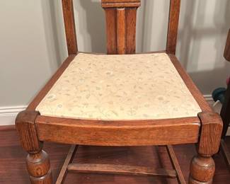 Carved Oak Dining Chair — Solid carved oak dining chair with turned front legs and decorative carved back splat. The seat is upholstered in a light floral patterned fabric; wood finish shows normal surface wear and small scuffs consistent with age but is structurally sound. Classic farmhouse/early 20th-century style suitable as a single accent or as part of a set; sash stretcher adds stability. See photos for detailed condition and upholstery pattern.