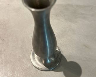Pewter Bud Vase — Simple pewter bud vase with a narrow trumpet top and flared base, clean-lined and suitable for a single stem or small arrangement. Solid, unmarked metal finish shows light surface wear and minor scuffs consistent with age and use but no dents that affect form. Compact decorative piece that works on a mantel, shelf, or in a bathroom; measures small and is easy to display. No maker's marks visible in photos.