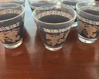 Grape Pattern Glasses Set — Set of six tapered drinking glasses with a black band and silver grape-and-vine decoration beneath a silver scroll border. Each glass has a slightly flared rim and thick base; decoration shows light surface wear but no chips or cracks visible in photos. Attractive mid-century cocktail or juice glasses that work well as a matched set for dining-room service or bar display. Sold together as pictured.