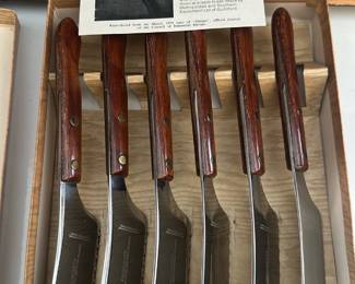 Prongsta Wood-Handled Steak Knives — Set of six Prongsta wood-handled steak knives in a fitted wooden box. Each knife has a full-tang stainless blade with riveted wooden scales; blades show light surface marks consistent with storage but appear free of chips or nicks. Prongsta is noted on the accompanying card and the knives present as a matched set ideal for table service or gift use. Box and knife handles show light wear and patina consistent with age; blades would benefit from a polish before use.
