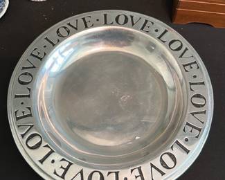 Pewter LOVE Rim Bowl — Heavy pewter decorative bowl with a wide rim engraved repeatedly with the word "LOVE" separated by dots. The piece appears to be pressed pewter with visible maker's marks on the underside and light surface wear and small scratches consistent with use. Solid, substantial tabletop or decorative serving bowl; rim lettering gives it a modern, giftable feel. Good overall condition with expected surface patina and no visible deep dents.