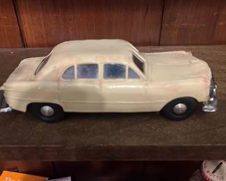 Beige Metal Toy Sedan Car — Small beige metal toy sedan with diecast-style body and metal chassis. Four rubber tires on axle rods and chrome-plated bumpers show light surface wear and paint chips consistent with play or display age. Solid construction with no broken parts visible; underside has stamped metal chassis with simple axle mountings. Good for collectors of vintage toy cars or as a display piece on a shelf.
