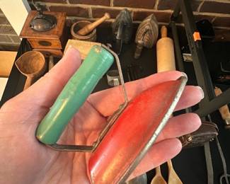 Child's Toy Sad Iron — Small vintage child's toy sad iron with a painted red metal body and green wooden handle. The piece appears to be a miniature reproduction of an old flat iron, likely intended as a child's toy or display prop; metal shows surface wear and light oxidation while the handle paint has minor chips. Solid, simple construction measures like a small handheld decorative iron and would suit collectors of vintage toys or kitchenalia. Sold as-is with visible cosmetic wear.
