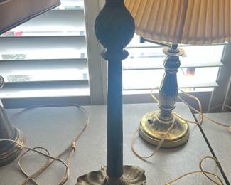 Brass Leaf Base Table Lamp — Brass table lamp with a decorative leaf-shaped base and slender column topped by a fabric shade. The lamp shows an aged brass patina consistent with regular use and has intact wiring visible in the photos; shade has light discoloration from use. Sturdy weighted base and classic traditional styling make it suitable for a desk or side table. Measures modestly and is ready to be tested for operation or rewiring if desired.