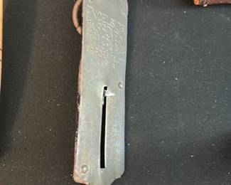 hanging spring scale — Small vintage hanging spring scale with a metal case, sliding indicator and large iron S-hook. The face shows stamped text (worn but present) and the body has surface rust and patina consistent with age and use. Functional condition unknown — spring mechanism may require cleaning or calibration; good for display or restoration as a workshop or farmhouse accent. Compact, handheld size with visible wear and one bent hook end.