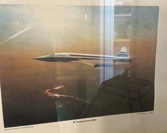 Concorde Framed Print — Framed Concorde aviation print showing the supersonic airliner in flight with sunset tones and a white mat within a simple black frame. The image is labeled "Concorde" at the lower margin and credits to "British Aircraft Corporation" are visible; frame shows light surface scuffs and the mat/glass have reflections as photographed. Ready to hang as shown — ideal for an aviation enthusiast or office decor.