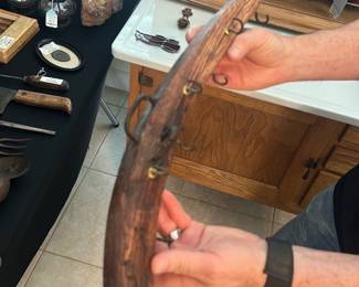 Wooden Yoke with Brass Hooks — Curved antique wooden yoke or harness beam fitted with multiple brass-ringed hooks and an iron carry handle; heavy, well-weathered patina with deep grain and age cracks visible. Likely used for hanging tools, harnesses, or as a barn/stable fixture, the piece shows honest wear consistent with long use but appears structurally intact aside from surface splits and oxidation on the metal hardware. Good rustic display or decorative restoration piece for farmhouse or rustic decor; measures compactly and is easy to mount or repurpose. No maker marks or dates visible in photos.