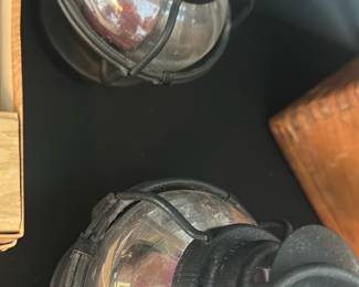 Pair Small Hanging Lanterns — A pair of small hanging lanterns with ribbed clear glass globes set in dark metal cages. Both have top vented caps with hanging loops; glass shows light surface wear and internal dust, metal has a worn patina consistent with age. Suitable as decorative indoor/outdoor accents or for conversion to electric; sold together as shown. Measurements are approximate from photos.