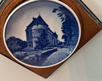 Wall Plaque Pair — Pair of blue-and-white Delft-style ceramic plaques set in diamond-shaped wood frames, perfect for living room wall display. Each round ceramic tile features classic Dutch scenes — a windmill and a castle/keep motif — set into stained wood diamond frames with a dark outer edge. Overall each framed plaque measures approximately 6 in square and projects about 1 in from the wall; lightweight and easy to hang. Both are in good condition with normal surface wear and light scuffs to the wood frames consistent with age.
