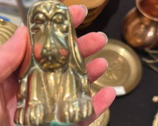 Brass Sitting Dog Figurine — Small solid brass dog figurine in a seated pose with stylized features and a greenish patina at the base. Heavy for its size and suitable as a paperweight or shelf accent; the piece shows age-related surface wear and light verdigris at the bottom edge as seen in the photos. Unmarked in images and measures compactly, a decorative brass collectible in good vintage condition.