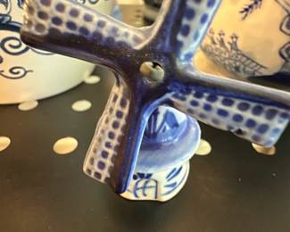 Blue White Ceramic Windmill Figurine — Small blue-and-white ceramic windmill figurine with hand-painted detail and a pierced center hub on the blades. Shown resting on a matching painted base, the piece has decorative Delft-style blue brushwork and a glossy glaze. Condition appears good with normal light surface wear and no obvious chips or cracks visible in the photos. Compact decorative accent appropriate for a shelf or collection of blue-and-white ceramics; see dimensions for size.