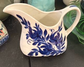 Crunchfield 1st Ed Handpainted Pitcher — Crunchfield handpainted cream pitcher from Erwin, Tenn., offered as a decorative small serving piece. The white ceramic body is decorated with blue floral motifs in a freehand style and has a single-loop handle and pronounced pouring spout; the base is marked "CRUNCHFIELD ANYWARE H. - HANDPAINTED ERWIN, TENN." (as shown). Good condition with visible crazing and light wear to the base consistent with age and use; no large chips or cracks visible in photos. Ideal for collectors of regional studio pottery or for use as a small creamer or bud vase; compact size makes it easy to display on a shelf or table.