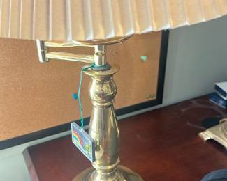 Brass Swing-Arm Table Lamp — Brass swing-arm table lamp with a pleated beige shade and adjustable arm. Solid turned brass column and weighted round base show light surface wear and tarnish consistent with normal use; wiring appears intact though lamp has not been tested for function. Classic polished brass finish works well for desk or bedside use and the adjustable arm adds practical reach. Shade measures approx. pleated beige paper style as shown; minor surface marks on base.