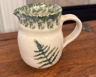 Dolores Reader Ceramic Fern Pitcher — Handmade ceramic pitcher signed by Dolores Reader, decorated with a green fern motif and a speckled green rim. Wheel-thrown form with a rounded body, pouring spout and loop handle; the base shows the artist's signature and a number (visible in photos). Good condition with light surface wear consistent with use and no visible cracks or chips. A decorative functional piece about the size of a small creamer or milk jug.