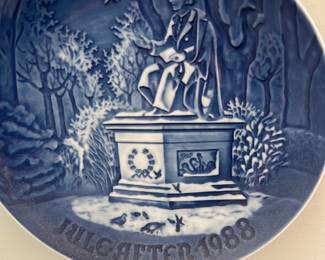 Bing & Grondahl 1988 Plate — This decorative 1988 collector plate from Bing & Grøndahl celebrates a winter scene with a seated figure on a plinth beneath a star. The plate is cobalt blue and white porcelain with raised relief detailing and 'JULGÅTFTER 1988' visible at the base. Ideal for wall display in a living room, it measures like a standard collector plate and is suitable for holiday or year-round collectors. Plate appears in good condition with no visible chips or cracks from the provided photos.