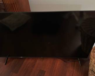 TCL LED Smart TV 43-inch — TCL LED smart TV with a slim bezel and paired TCL remote shown in photos. The TCL badge is visible on the front bezel and the remote includes streaming app shortcuts (Netflix, YouTube, Prime Video, Apple TV), indicating a Roku/Smart platform model. Good working condition is assumed from intact screen and accessory remote; minor surface dust and light scuffs on the lower bezel are visible. Measures approximately 43 inches diagonal (typical for this cabinet size); see dimensions below.